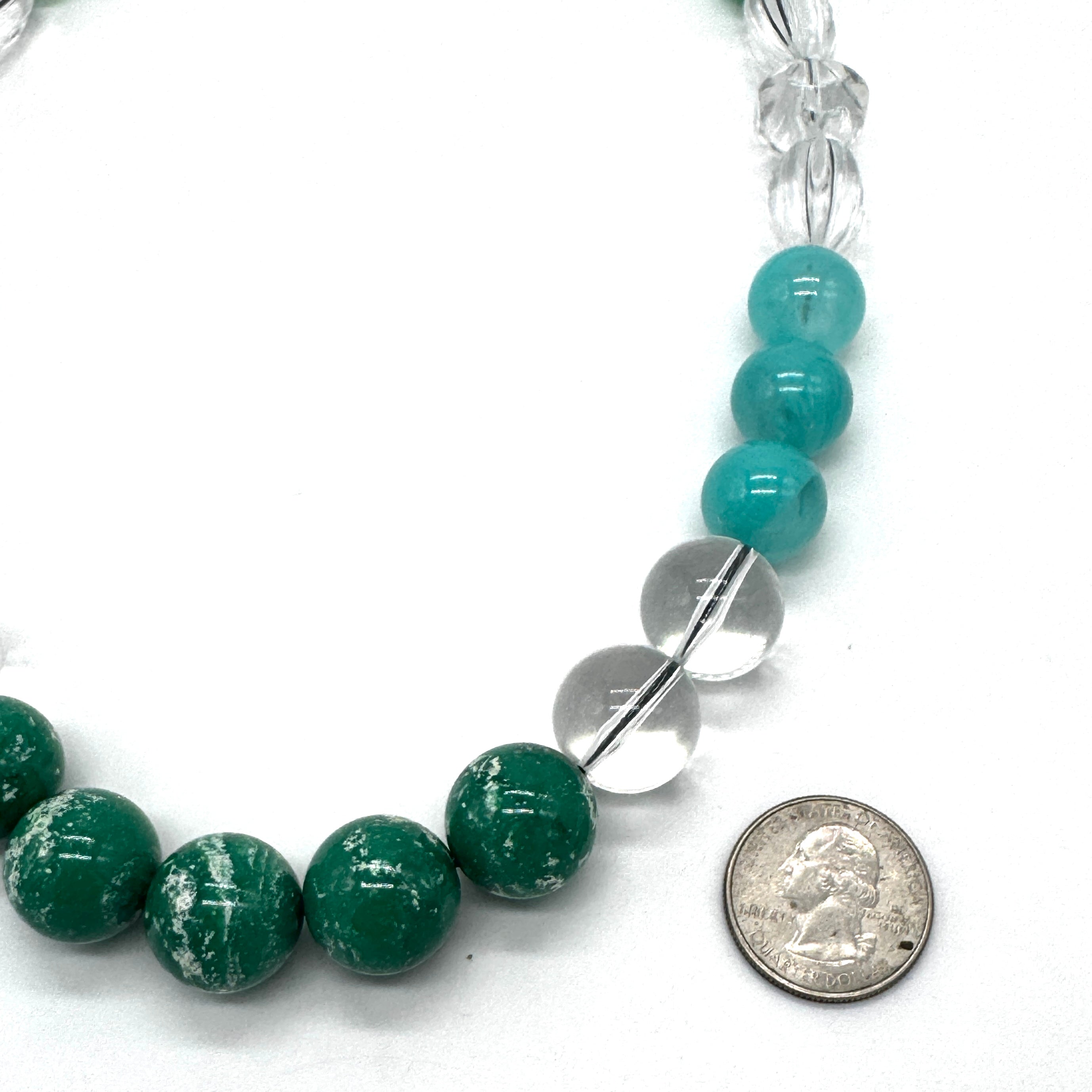Beaded necklace with green and clear beads, shown with a coin for scale on a white background