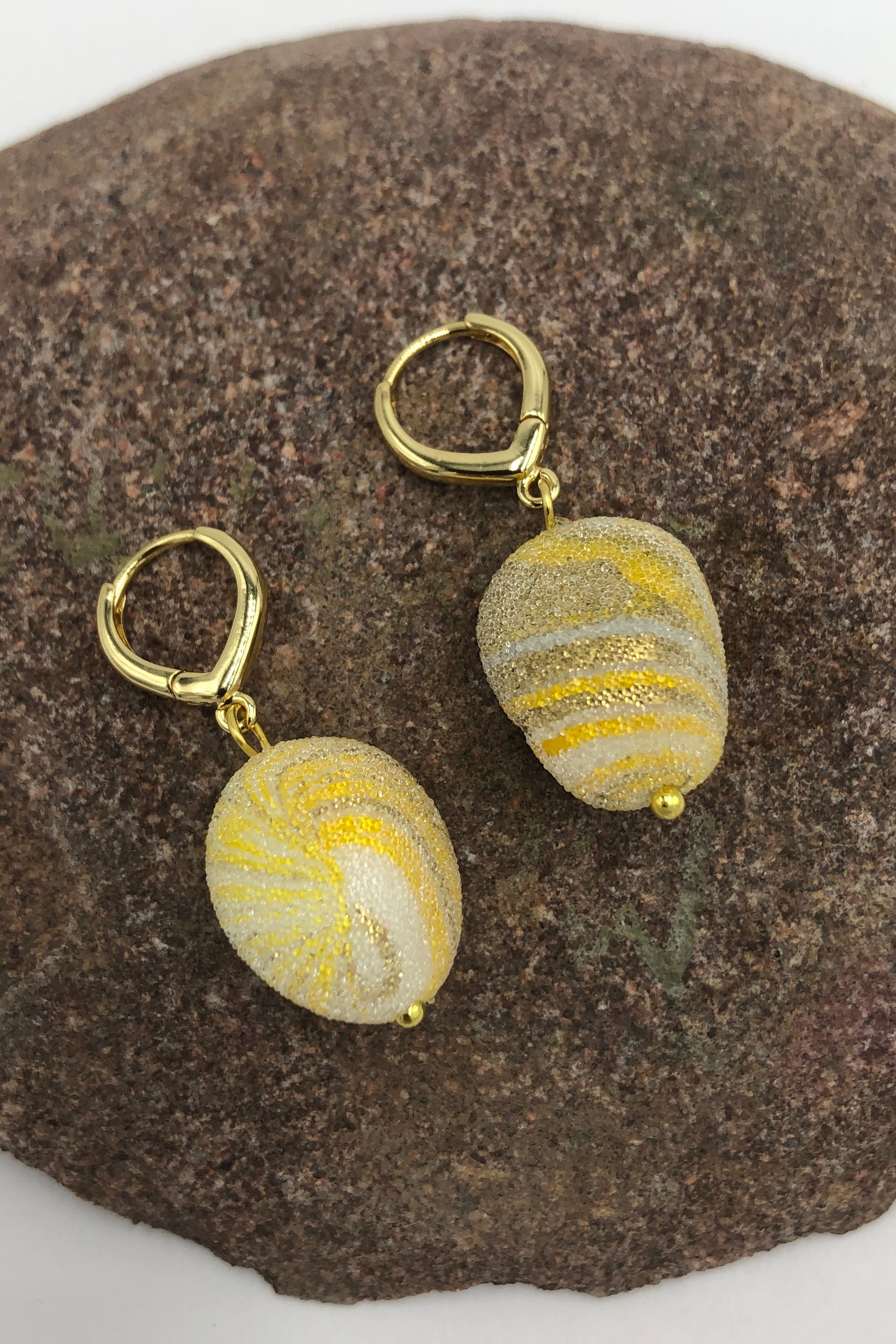 yellow and gold swirl earrings on a rock