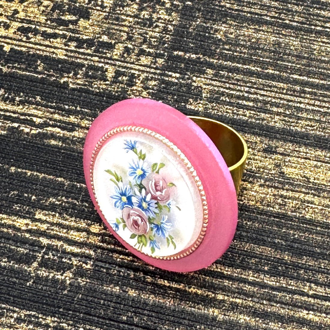 Circular cocktail ring with floral design on a textured black and gold background