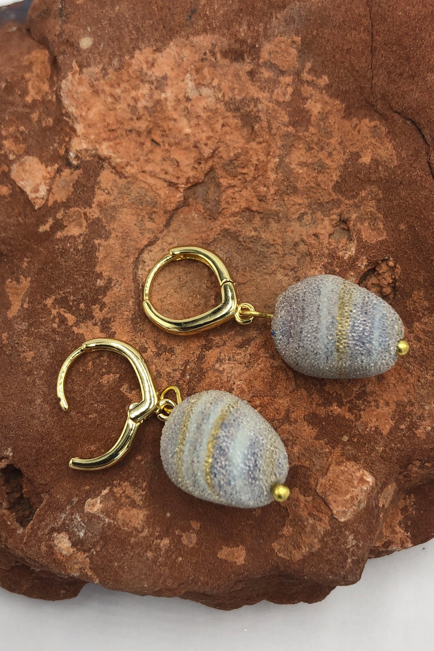 purple and gold swirl earrings on a rock
