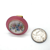 Large round pink ring with floral design next to a U.S. quarter coin on a white background