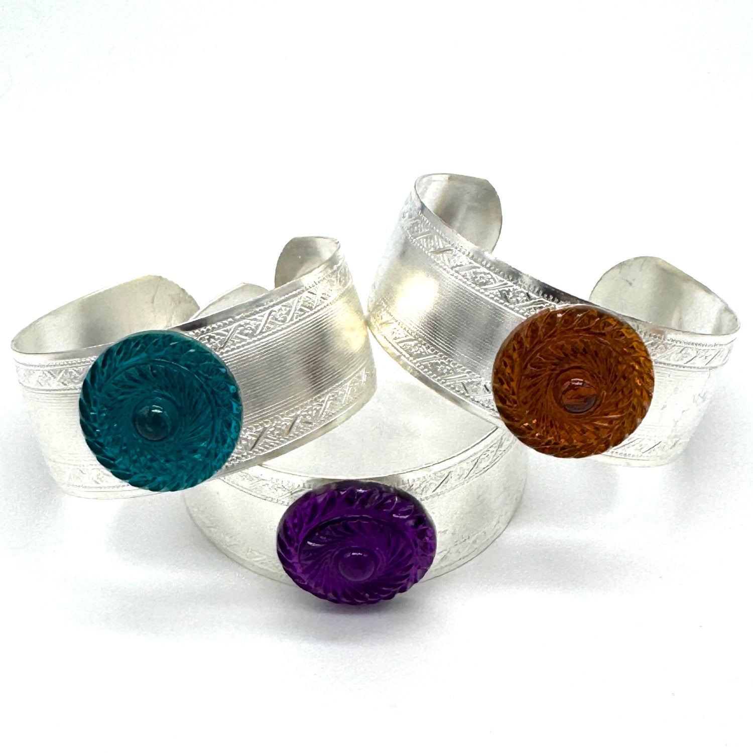 Three silver cuff bracelets with colorful lucite cabochons on a white background