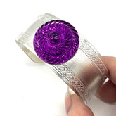 Silver bracelet with a purple lucite stone held by a hand on a white background