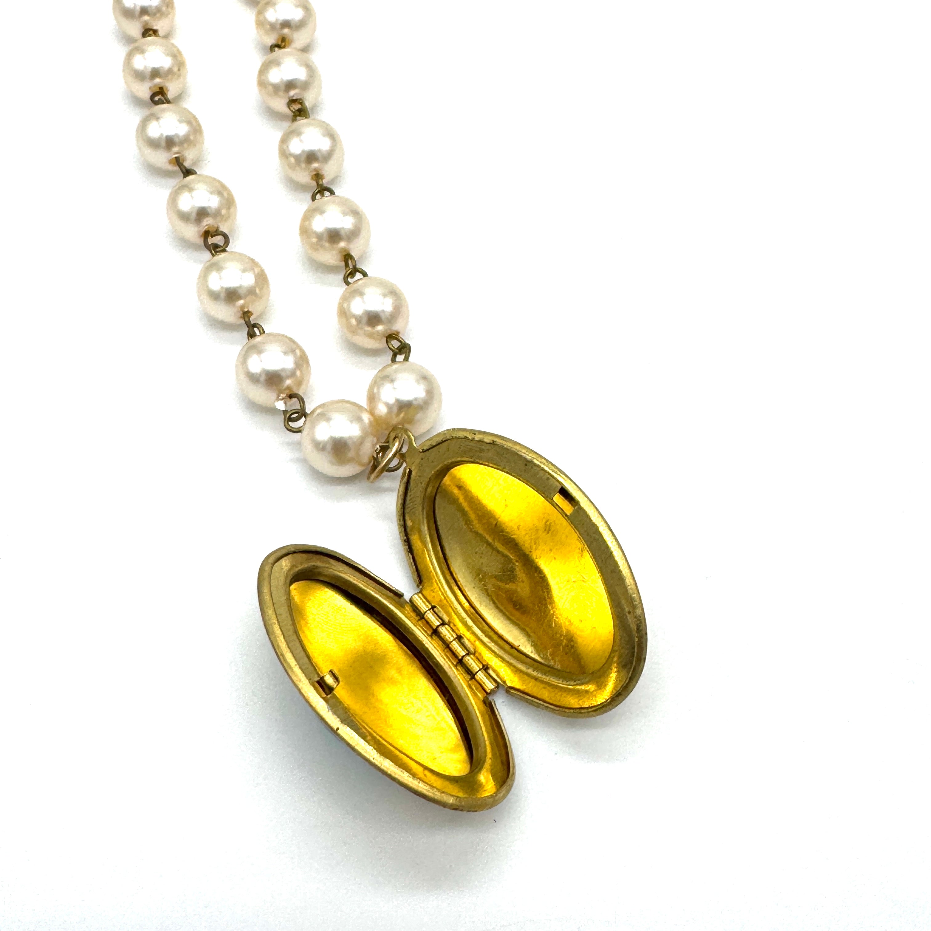 Gold locket with open face on a pearl necklace against a white background