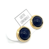 Gold-framed round earrings with dark blue centers on a white background, featuring the brand &