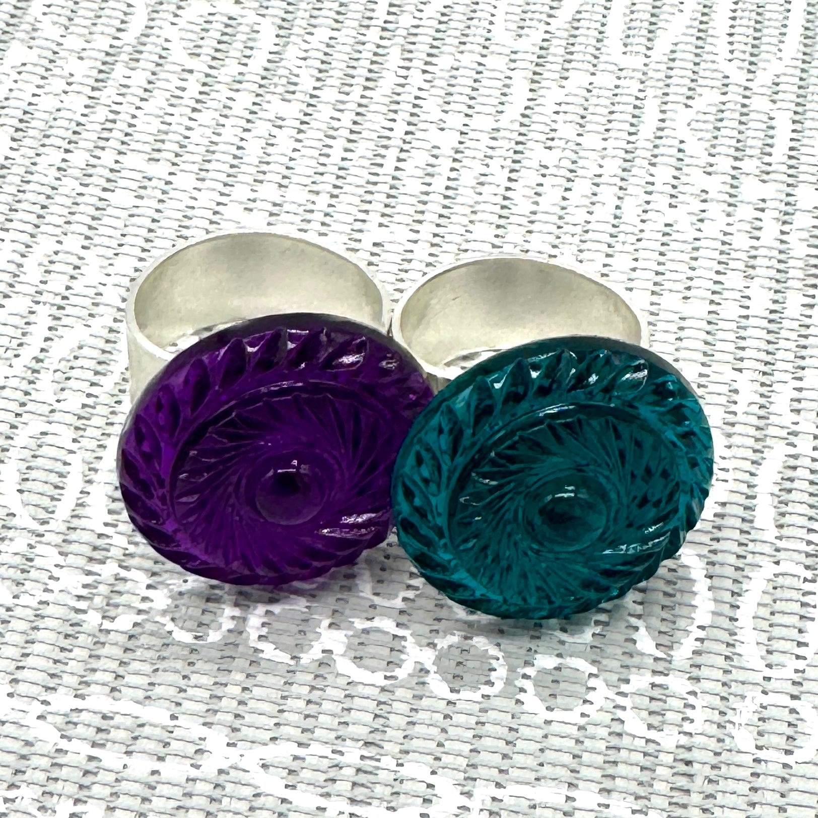 Two lucite cocktail rings, one purple and one teal, on a textured white background.