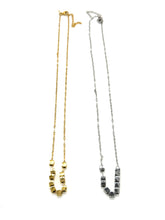 A pair of necklaces, in silver and gold, on a white background. Each is a fine chain with several cube beads at the center.
