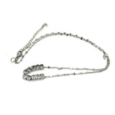 A silver necklace on a white background. It is a fine chain with several cube beads at the center.