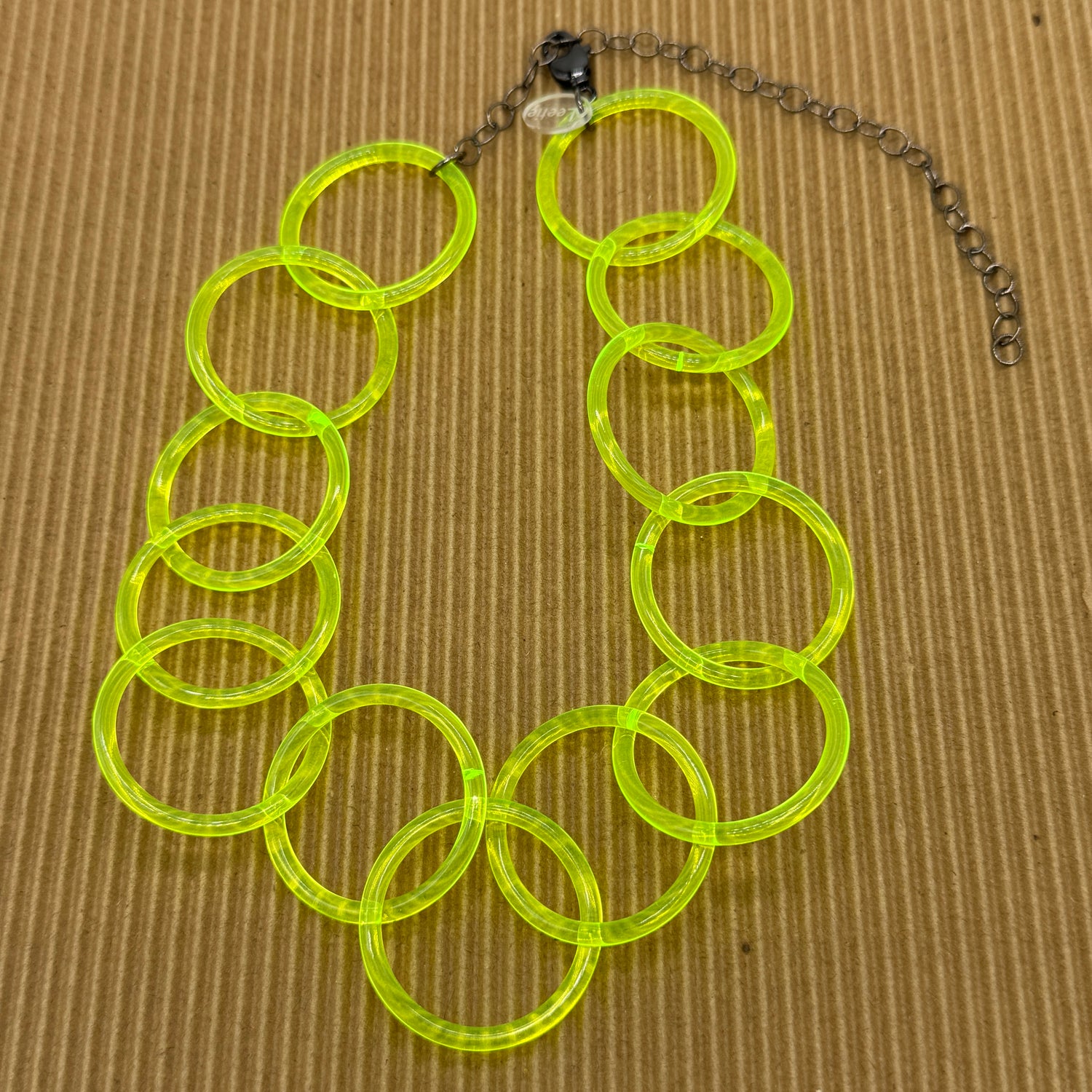 Adjustable necklace featuring large lucite chain links in a neon yellow on a brown background.