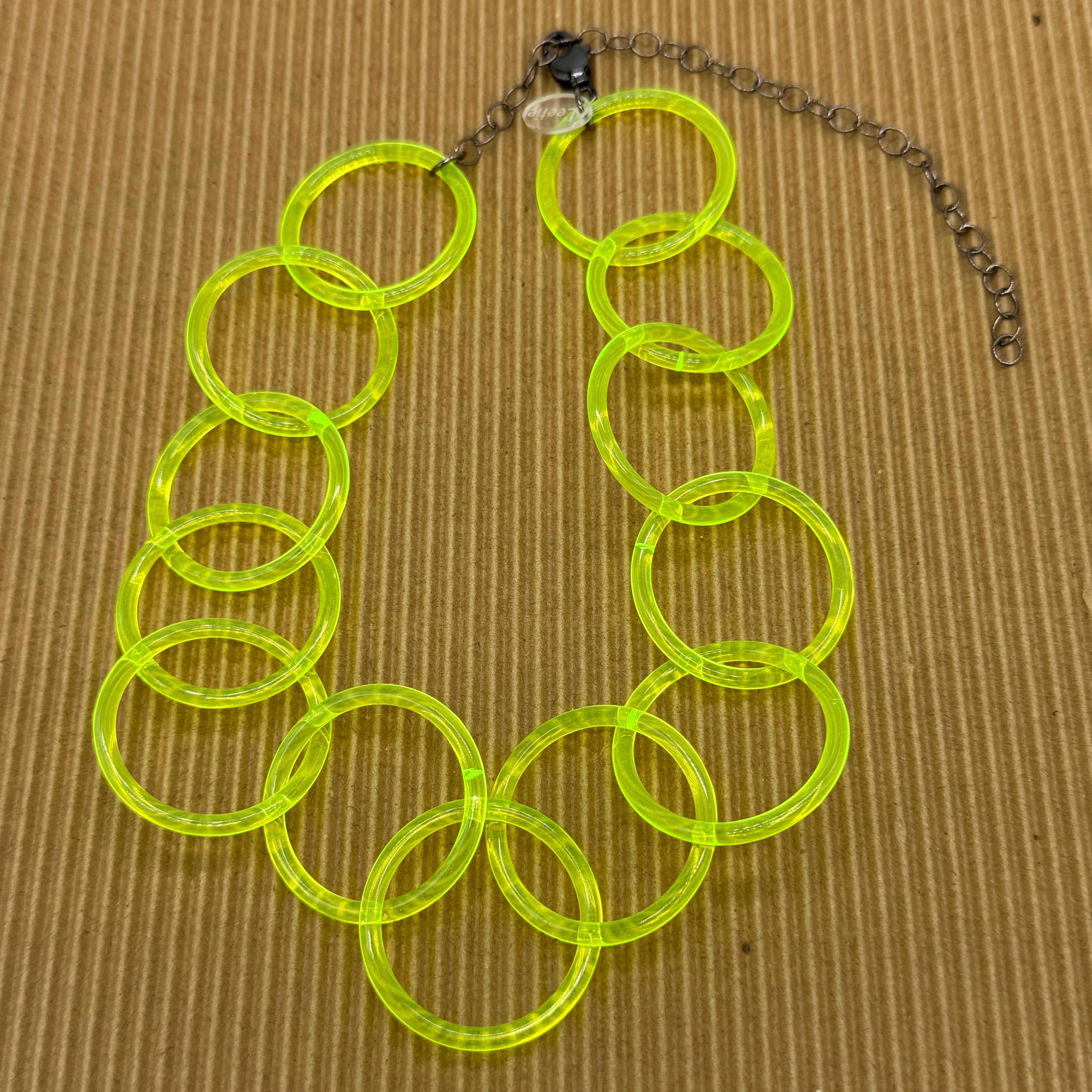 Adjustable necklace featuring large lucite chain links in a neon yellow on a brown background.