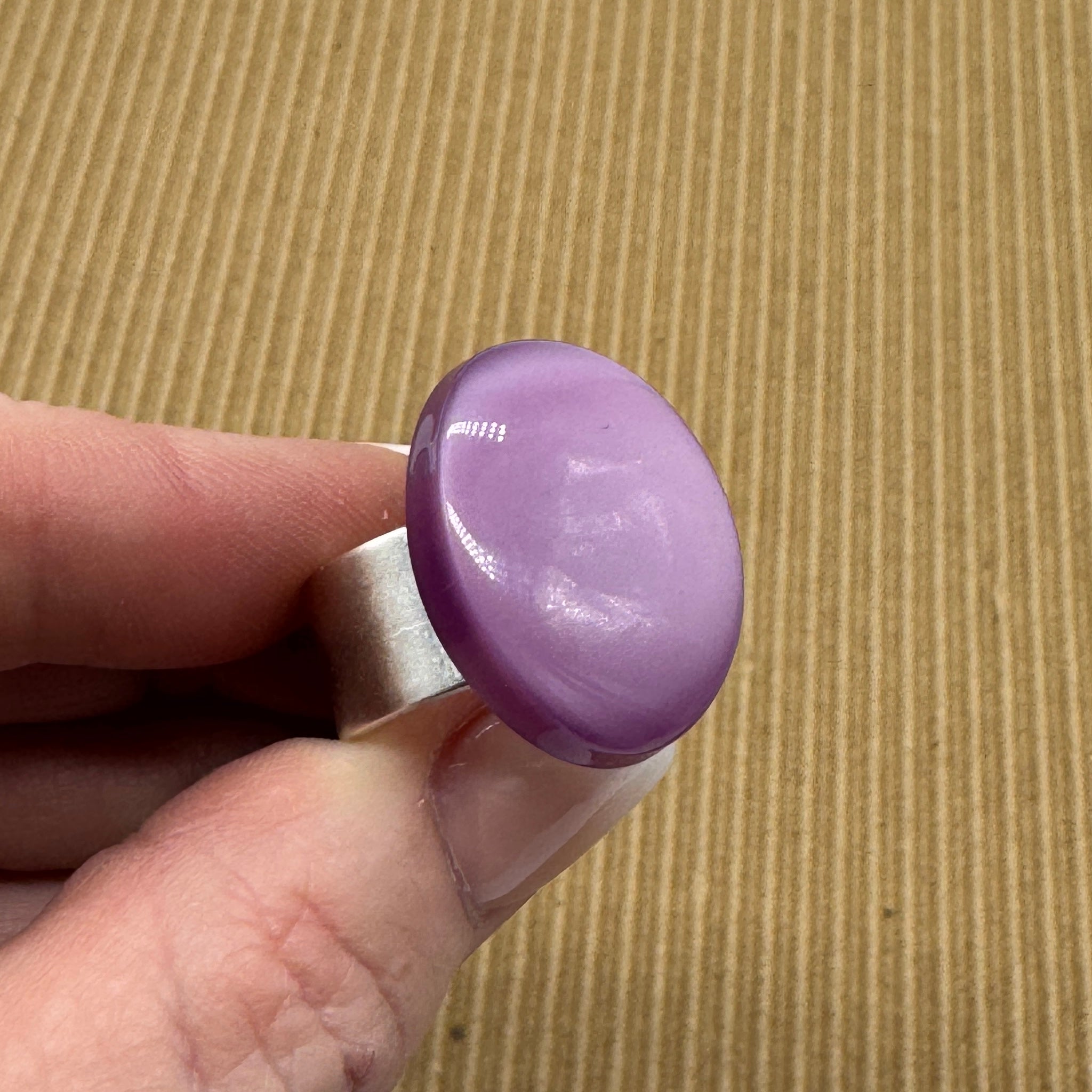Cocktail ring featuring large purple moonglow focal held by a hand over a brown textured background.