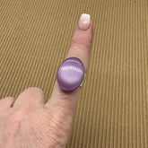 Cocktail ring on a finger featuring large purple moonglow focal on a brown textured background.
