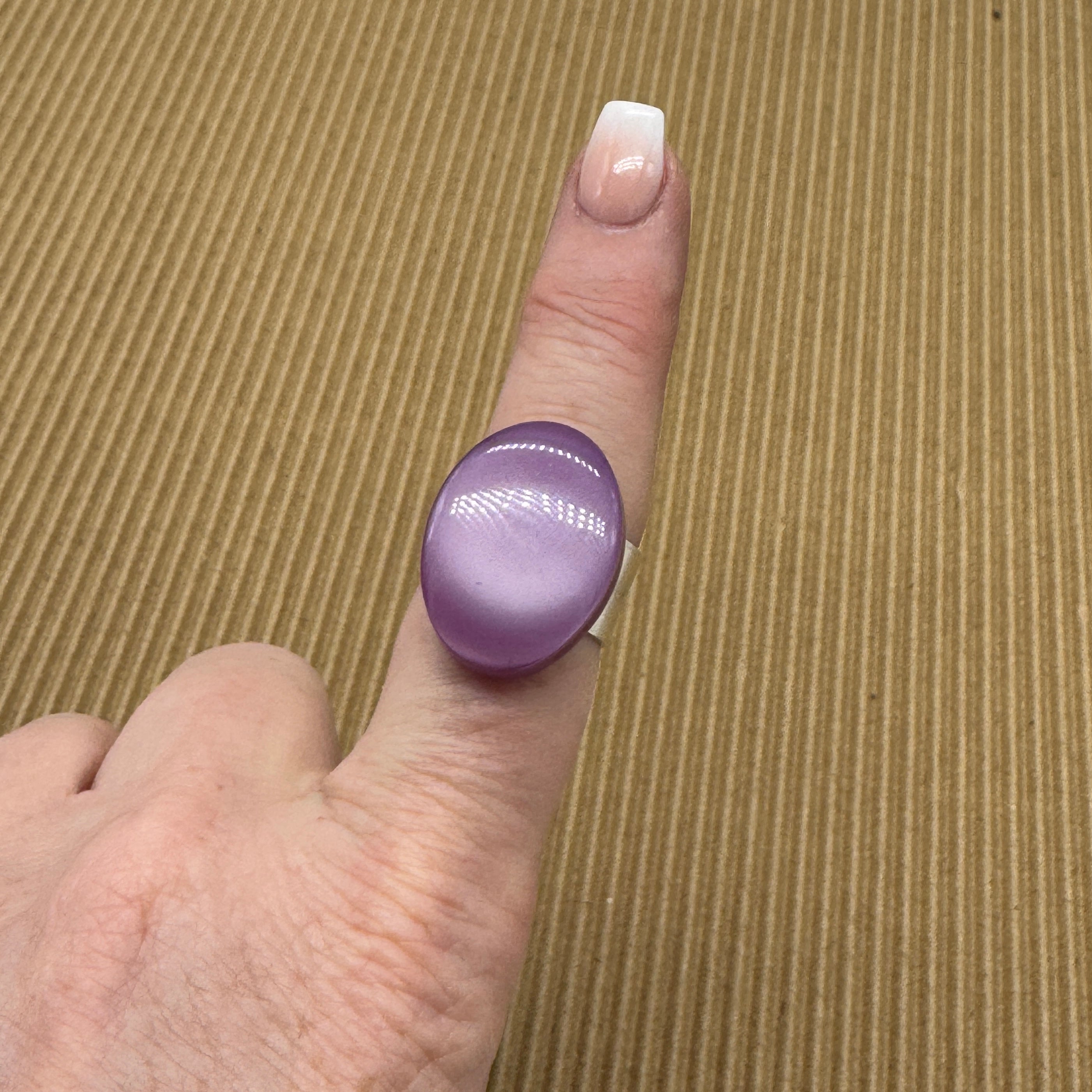 Cocktail ring on a finger featuring large purple moonglow focal on a brown textured background.