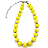 Adjustable necklace made of strung yellow moonglow lucite beads with small purple spacer beads on a white background.