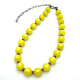 Adjustable necklace made of strung yellow moonglow lucite beads with small purple spacer beads on a white background.