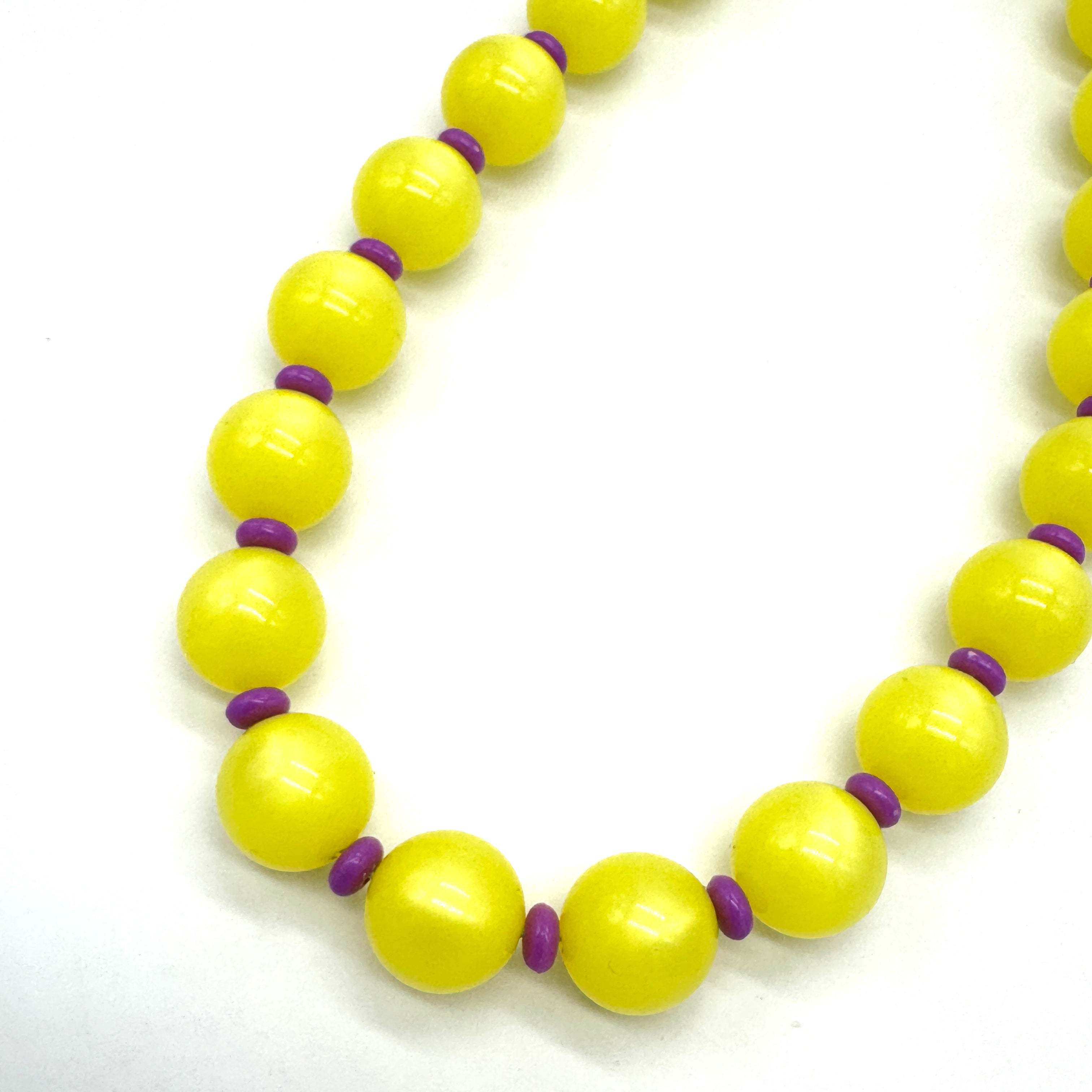 Close up of necklace made of strung yellow moonglow lucite beads with small purple spacer beads on a white background.