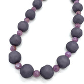 Closeup of necklace featuring dark gray and lilac lucite beads laid on a white background.