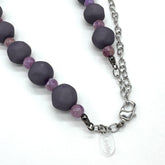 Closeup of adjustable necklace featuring dark gray and lilac lucite beads laid on a white background.
