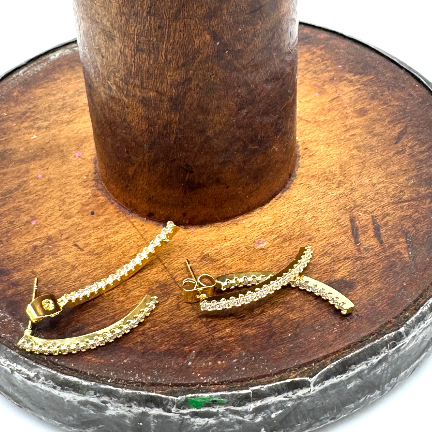 Golden stud earrings with an intersecting silhouette accented with sparkling cubic zirconias on a wooden stand.