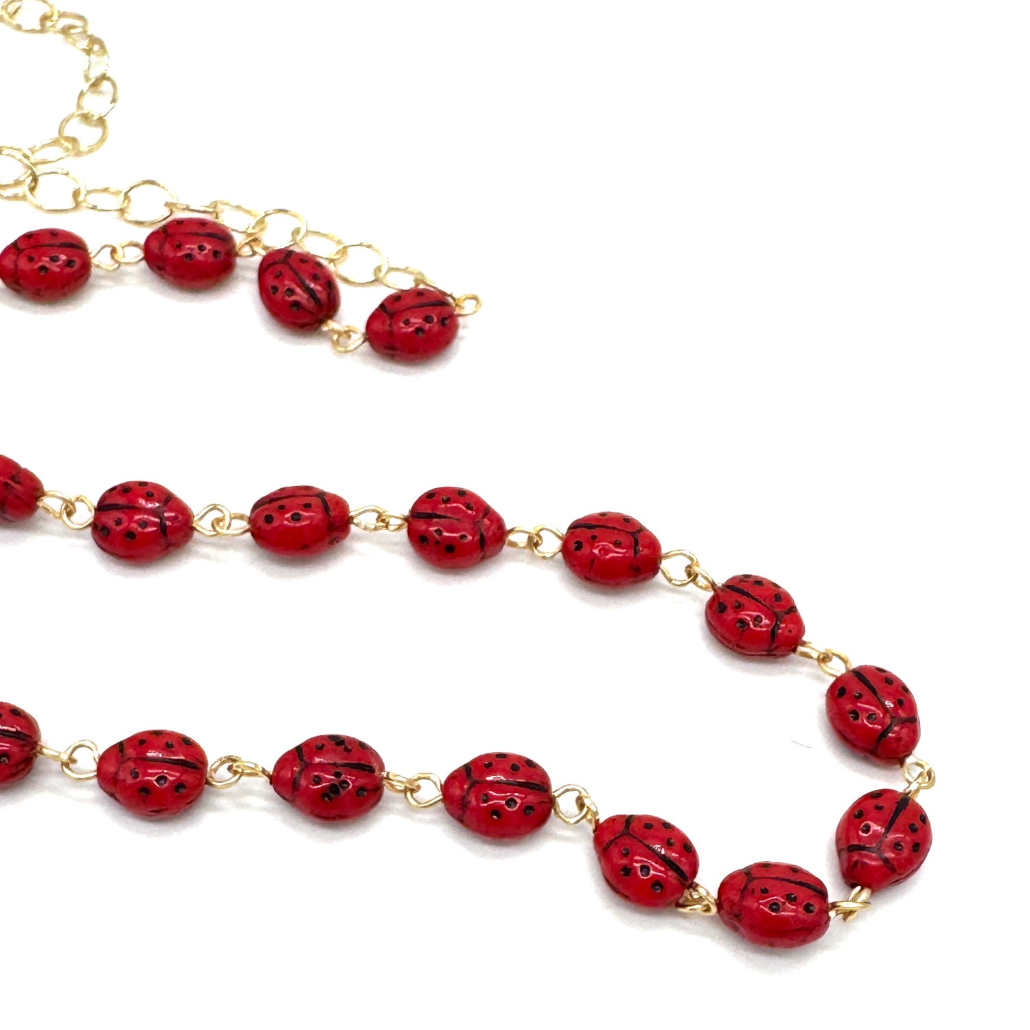 Necklace with red ladybug beads and gold chain on a white background