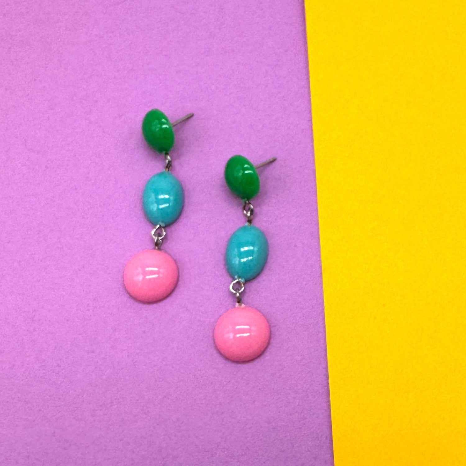 Pair of earrings with green, blue, and pink beads on a purple and yellow background