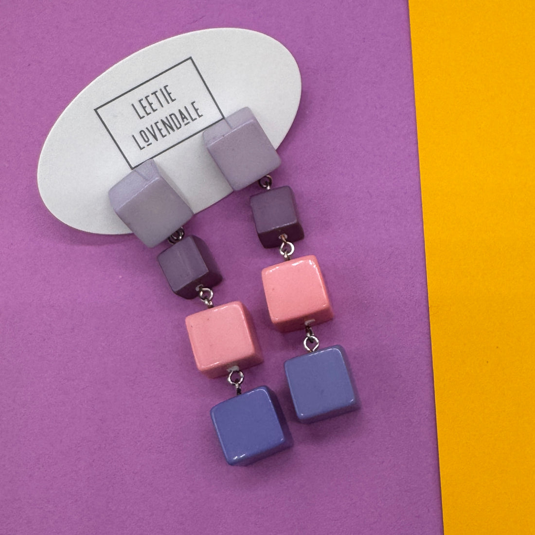 Colorful square earrings on a purple and yellow background with &