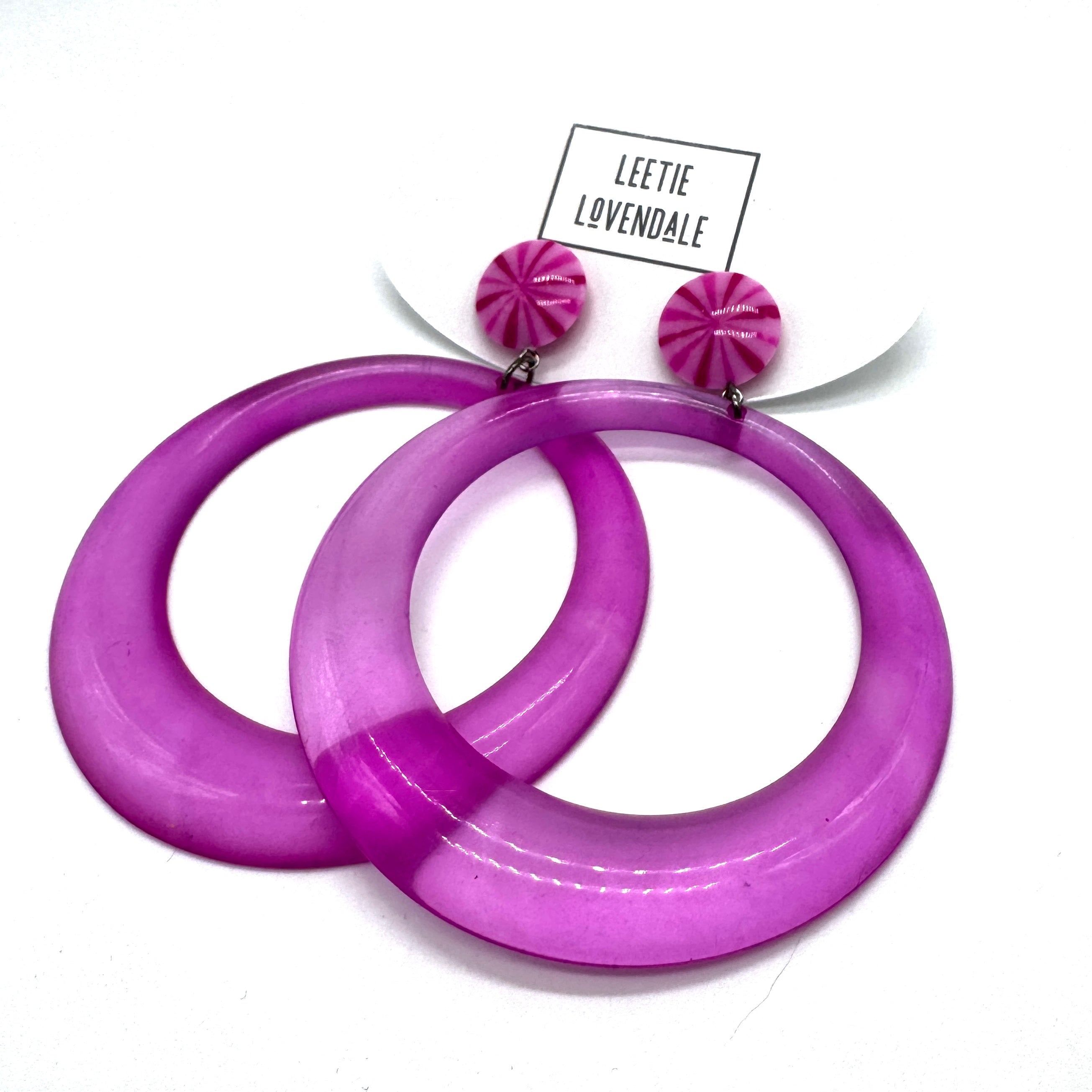Purple hoop earrings with pink top parts on a white background, featuring a brand label.