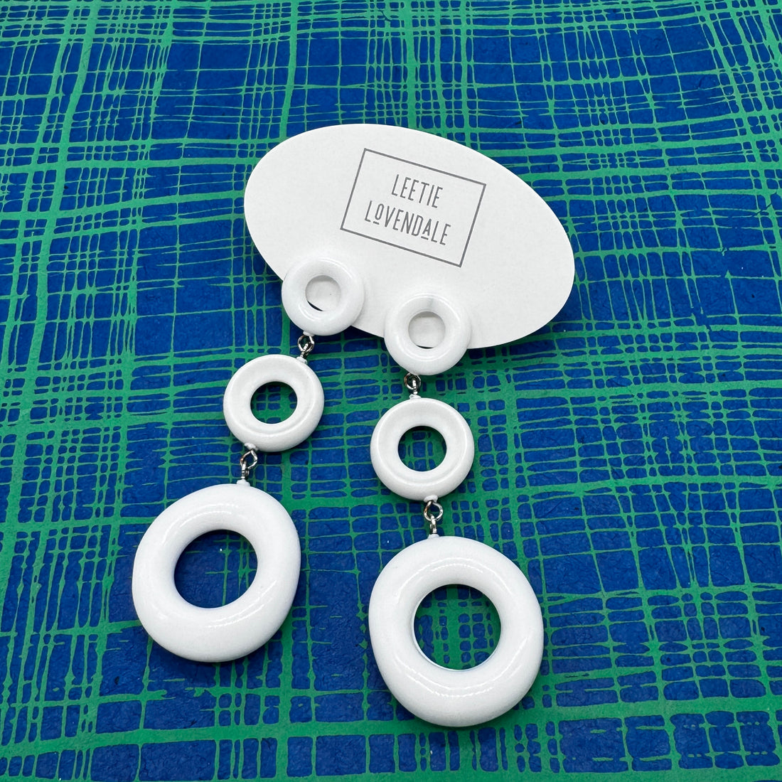 White circular earrings on a blue and green patterned background