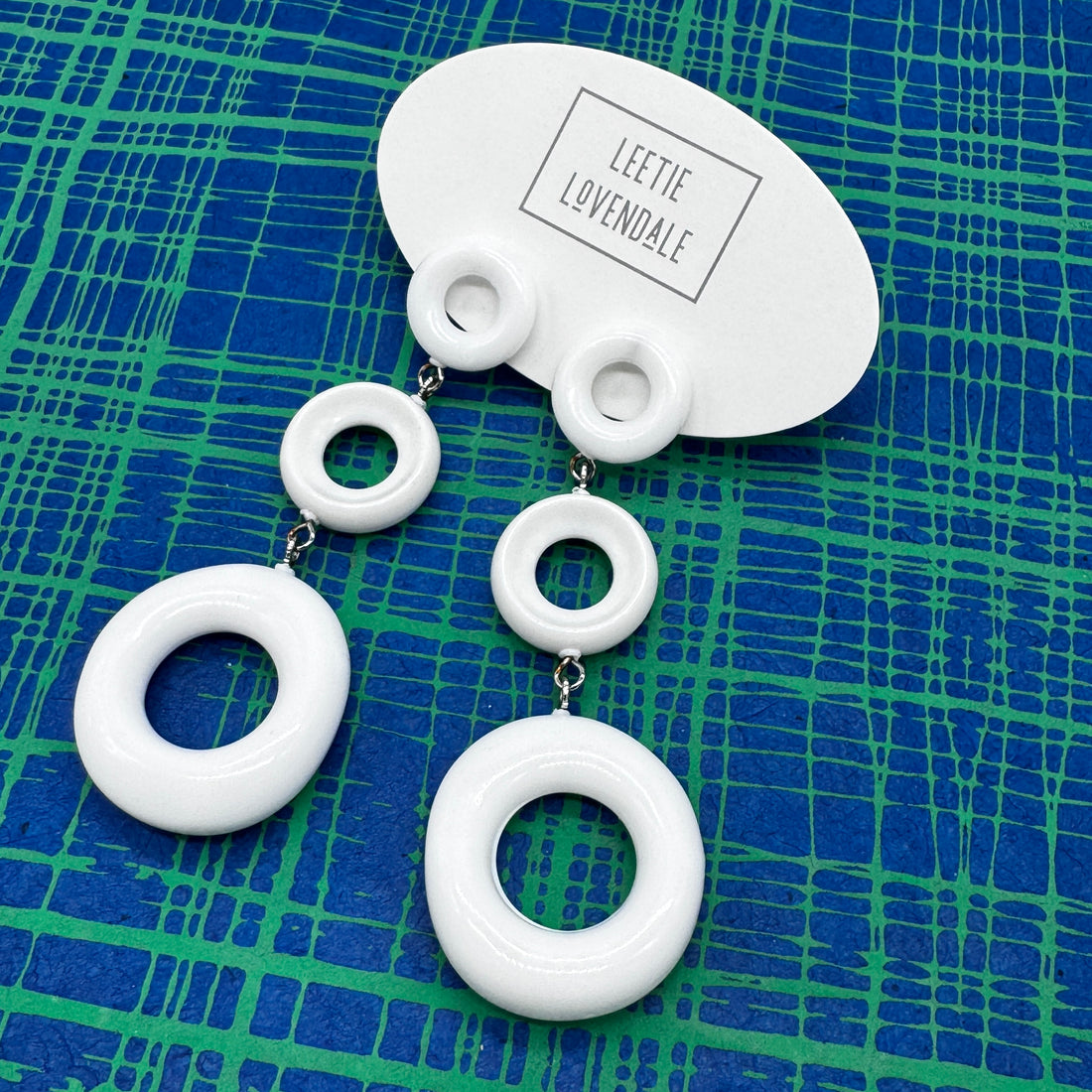 White circular earrings on a blue and green patterned background with &