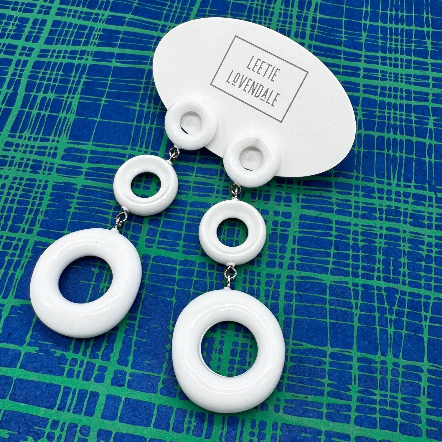 White circular earrings on a blue and green patterned background with &
