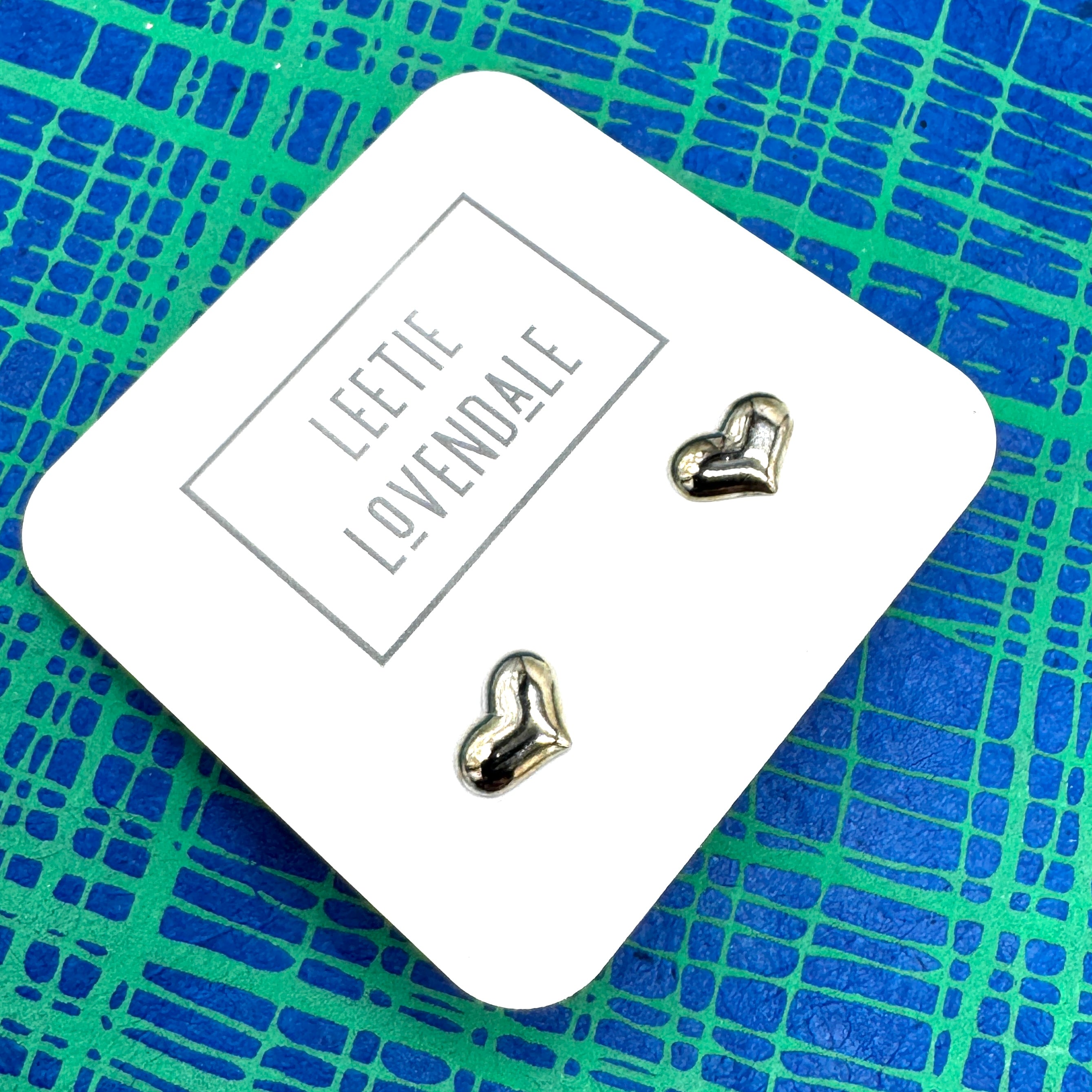Heart-shaped earrings on a branded card with a blue and green patterned background