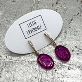 Purple earrings on a branded card with &
