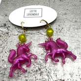 Pink unicorn earrings with green beads on a textured surface with &