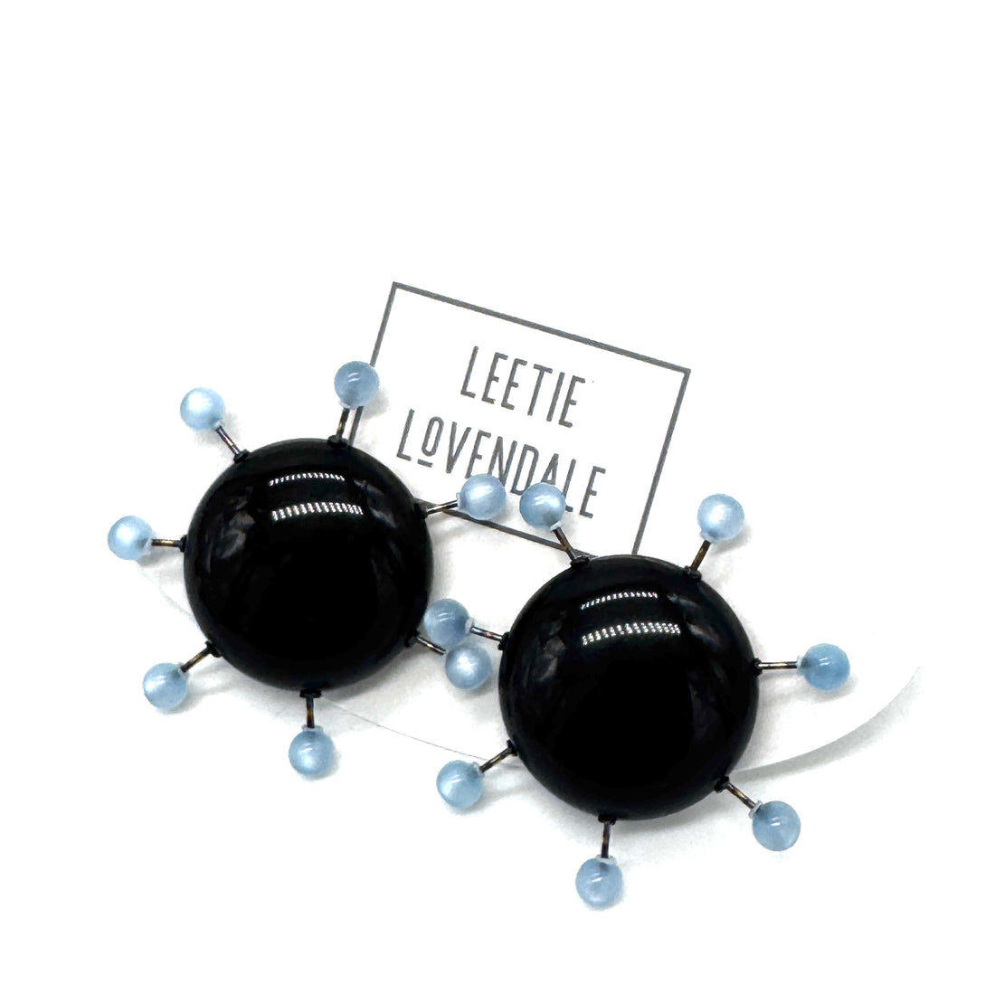 Black circular earrings with blue beads on a white background, featuring the brand &