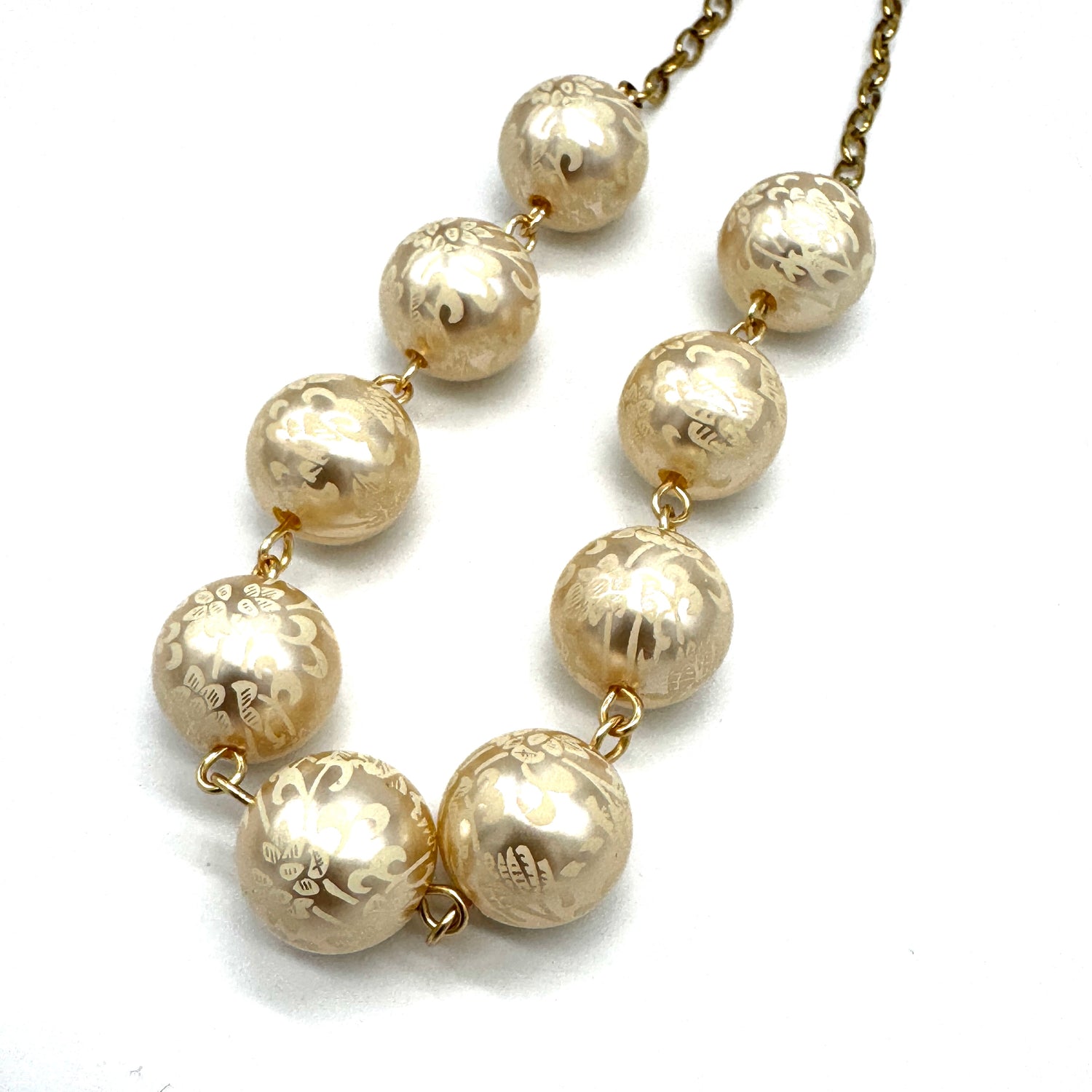 Closeup of half chain and half beaded necklace, featuring gold chain and floral etched pearl lucite beads.