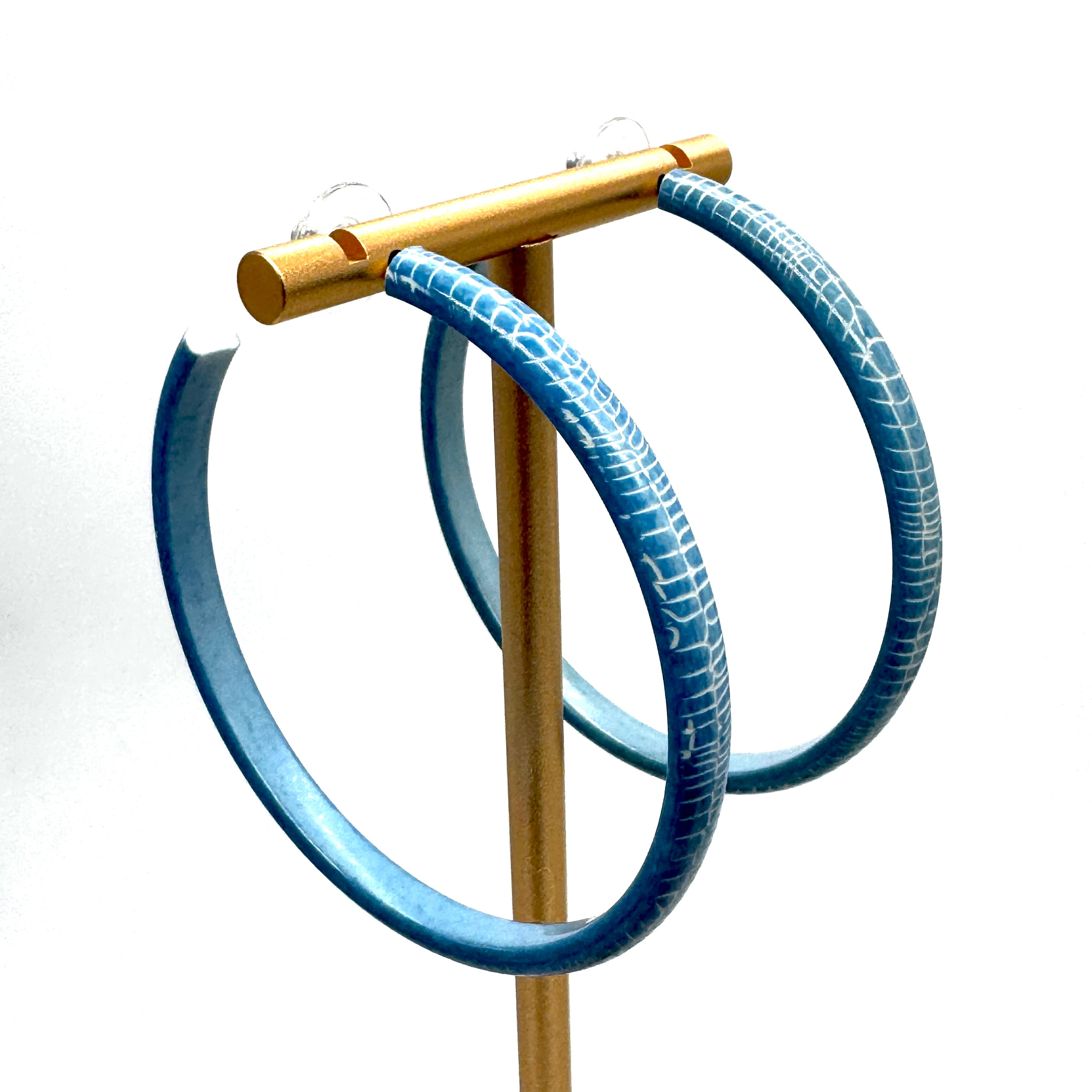 Large crackled blue lucite hoop earrings on a gold stand.