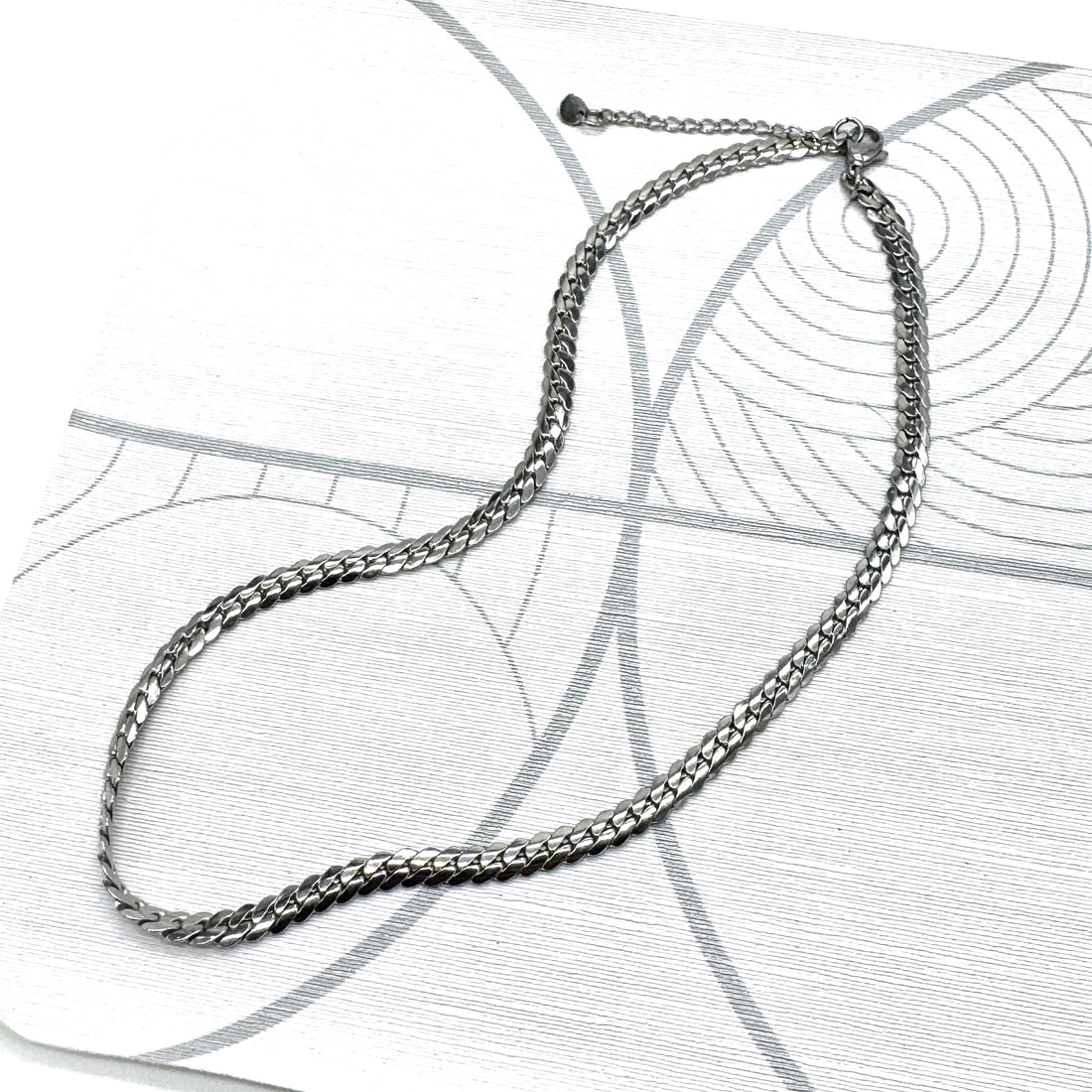 Adjustable silver snake chain necklace on a patterned background.