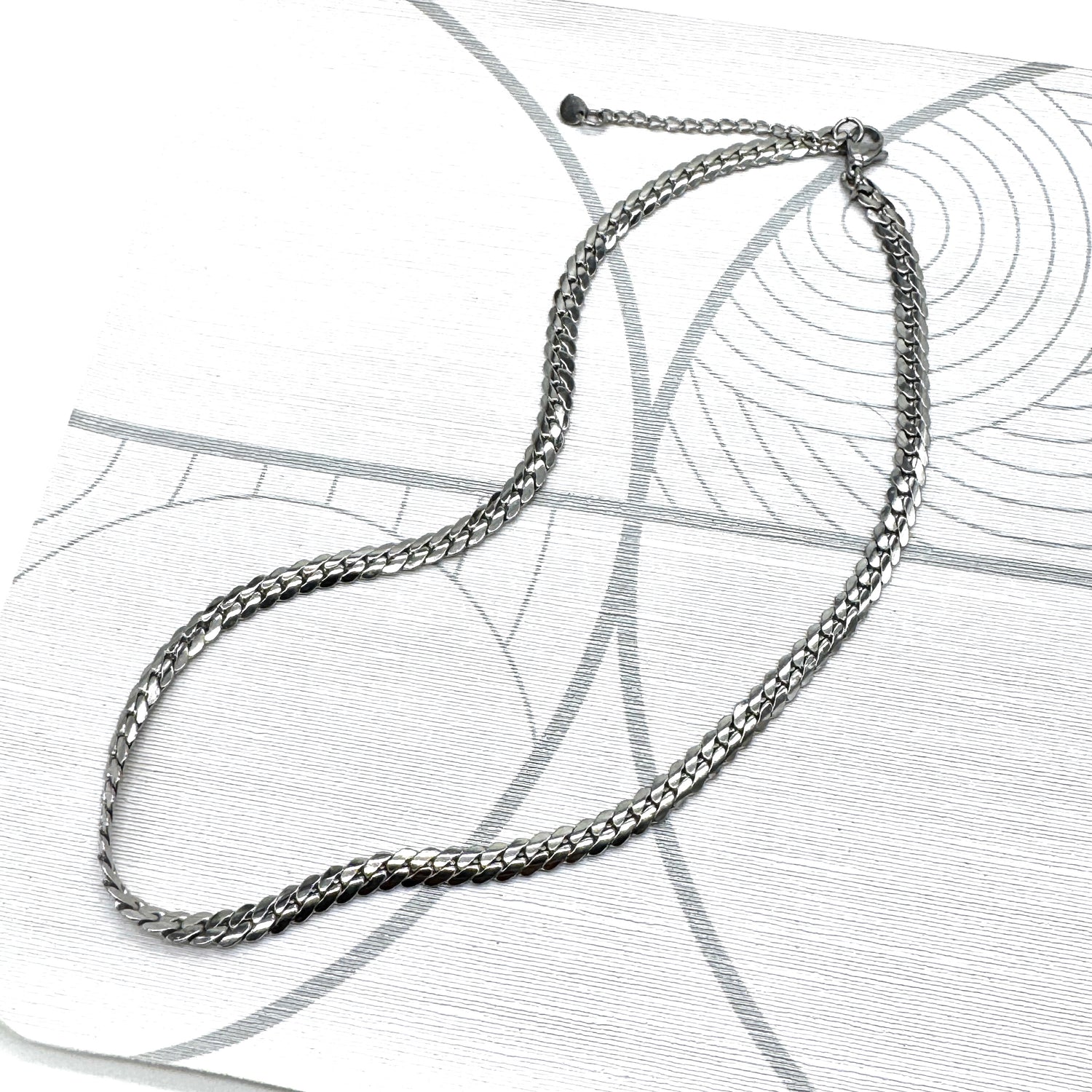 Adjustable silver snake chain necklace on a patterned background.