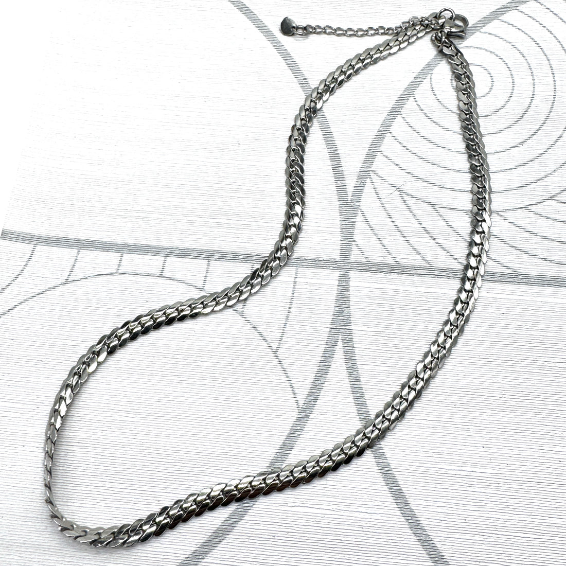Adjustable silver snake chain necklace on a patterned background.