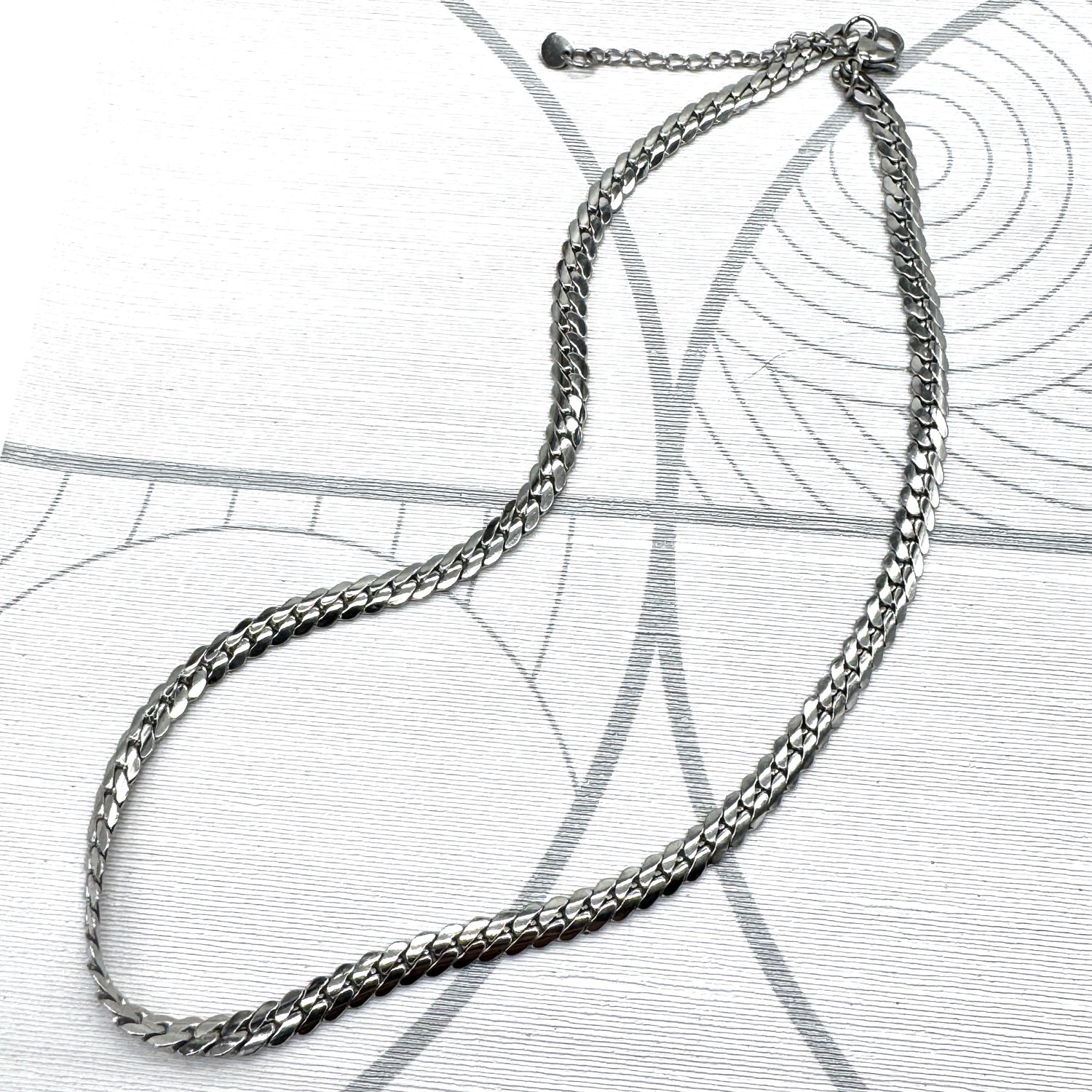 Adjustable silver snake chain necklace on a patterned background.