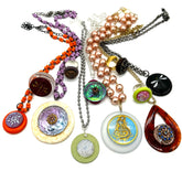 A collection of nine distinct handmade bead necklaces and pendants arranged on a plain white background. The jewelry features a variety of materials including orange beads, purple beads, faux pearls, silver chains, green and lavender beads, and colorful enamel medallions.