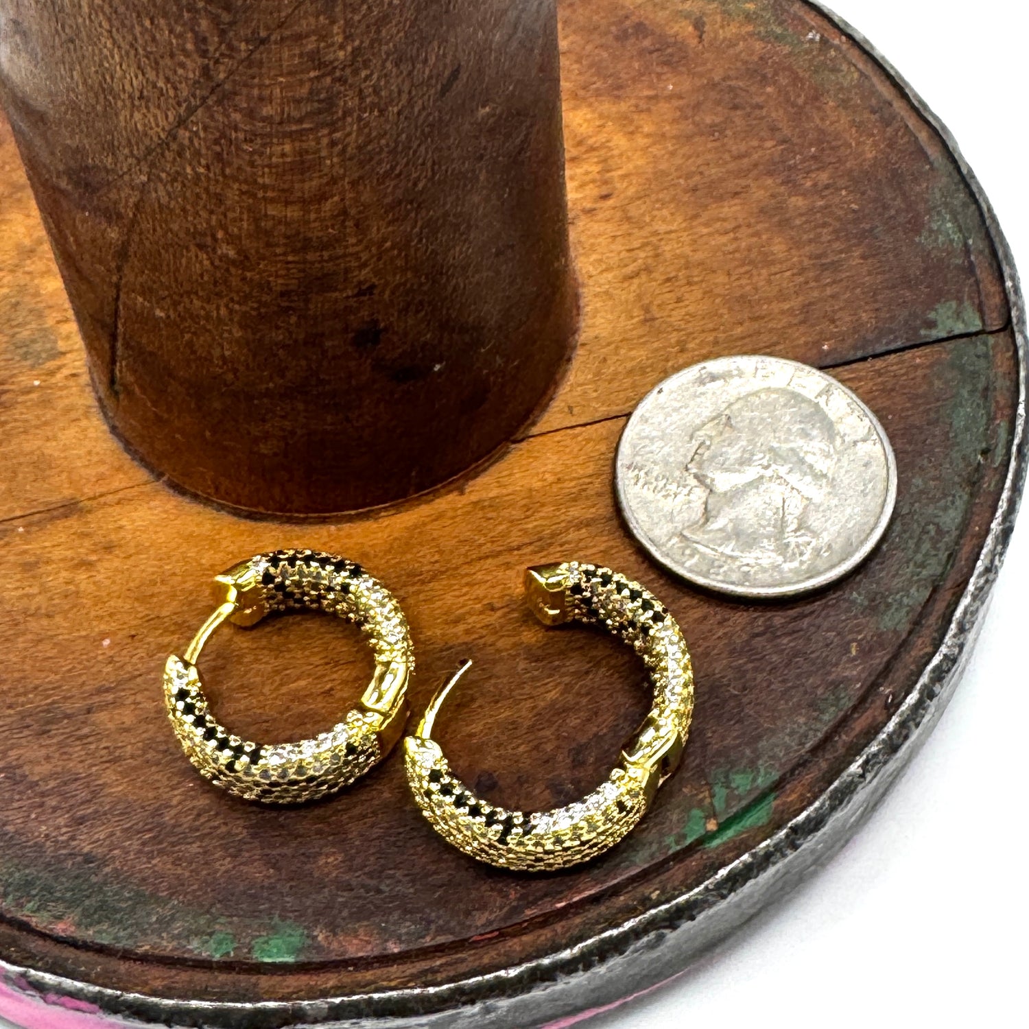 A pair of gold hoop earrings with a textured, snake-like scale pattern, displayed on a rustic wooden surface next to a US quarter coin for scale.