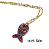 A gold chain necklace with a fish-shaped pendant featuring a vibrant fuchsia and pink pattern, shown on a white background with the text &
