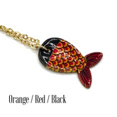 A close-up of a fish-shaped pendant necklace on a gold chain against a white background, with the text &