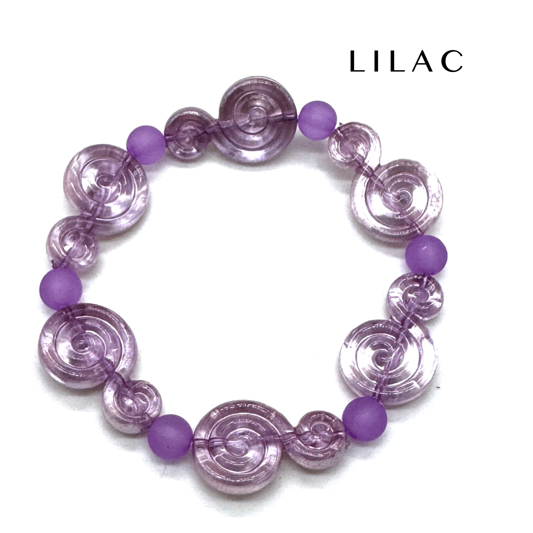 A lilac beaded stretch bracelet featuring translucent spiral-shaped beads and matte purple round beads, displayed on a clean white background with the brand name &