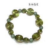 A beaded stretch bracelet featuring textured olive green spiral beads and matte sage green round beads, displayed on a clean white background with the brand name &