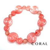 A coral pink beaded bracelet featuring large spiral-shaped beads and smaller round beads, displayed on a clean white background with the word &