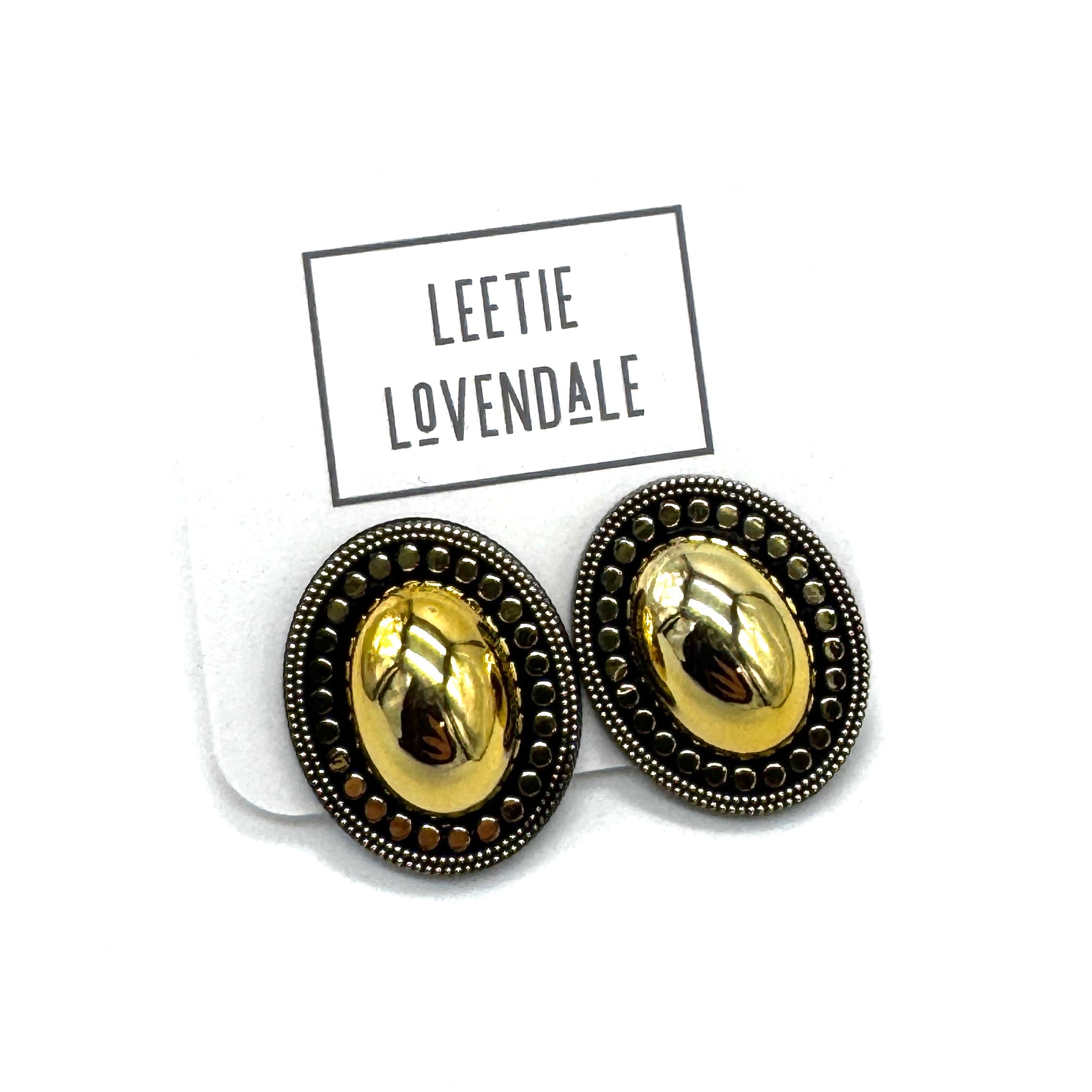 A pair of oval stud earrings with a shiny gold center and a dark bronze textured border, displayed on a white backing card with the brand name &