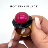 Hand holding a lip balm with a pink cap and black top, labeled &