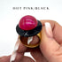 Hand holding a lip balm with a pink cap and black top, labeled &